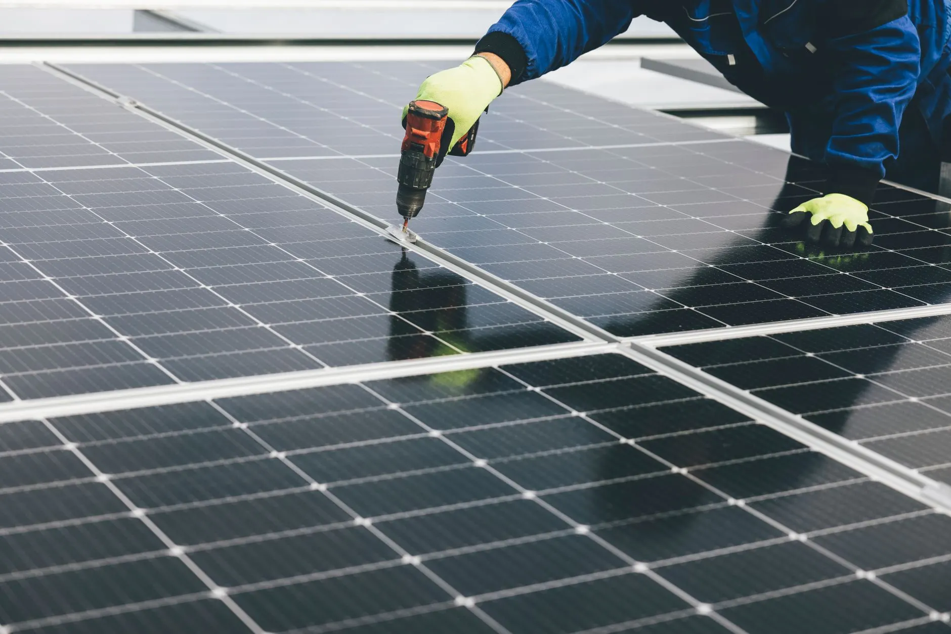 Monteur setzt mit dem Akkuschrauber eine Klemme zwischen zwei PV-Modulen