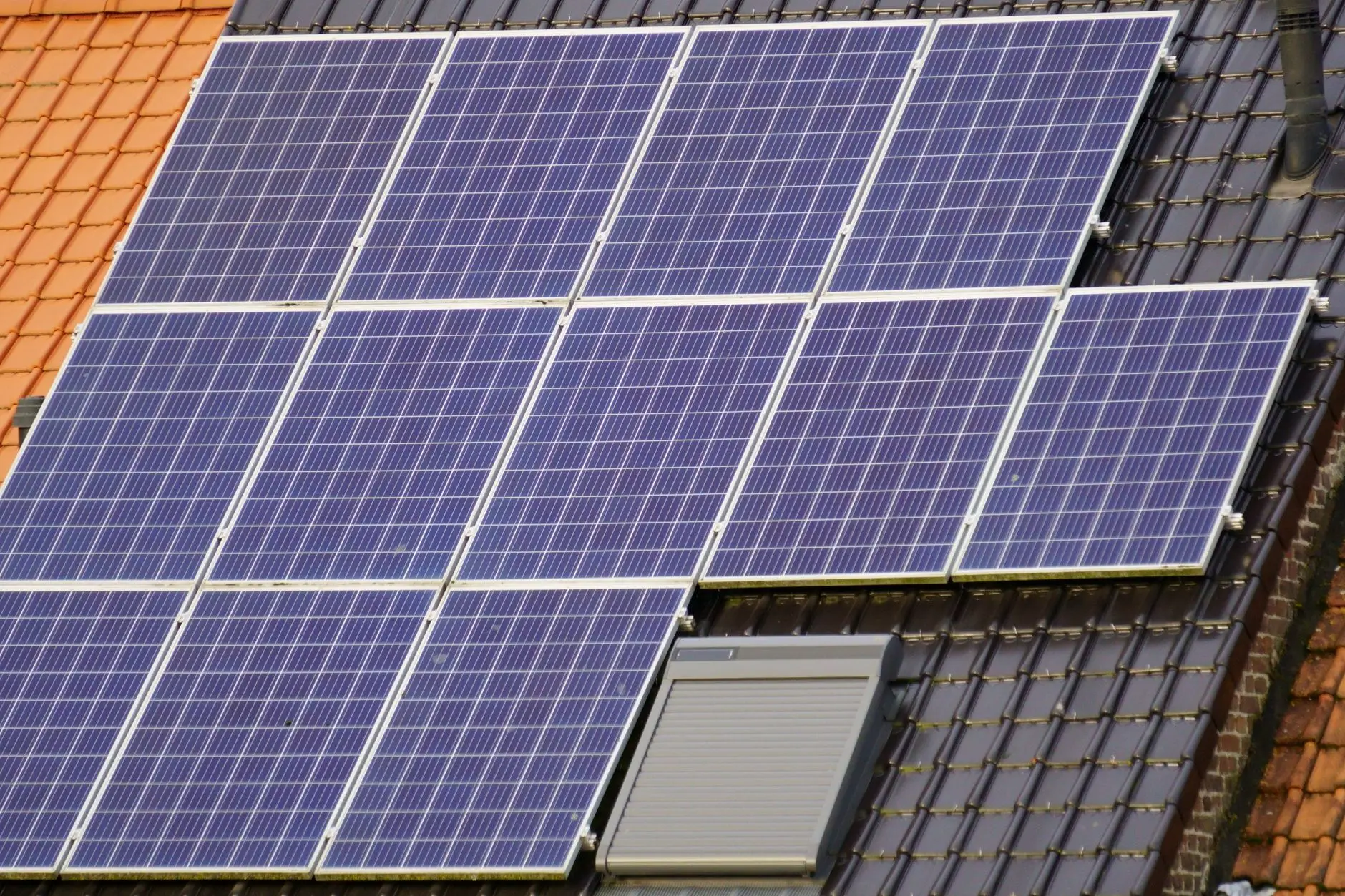 PV-Module auf einem dunkel gedeckten Dach neben einem Dachfenster mit Rollladen