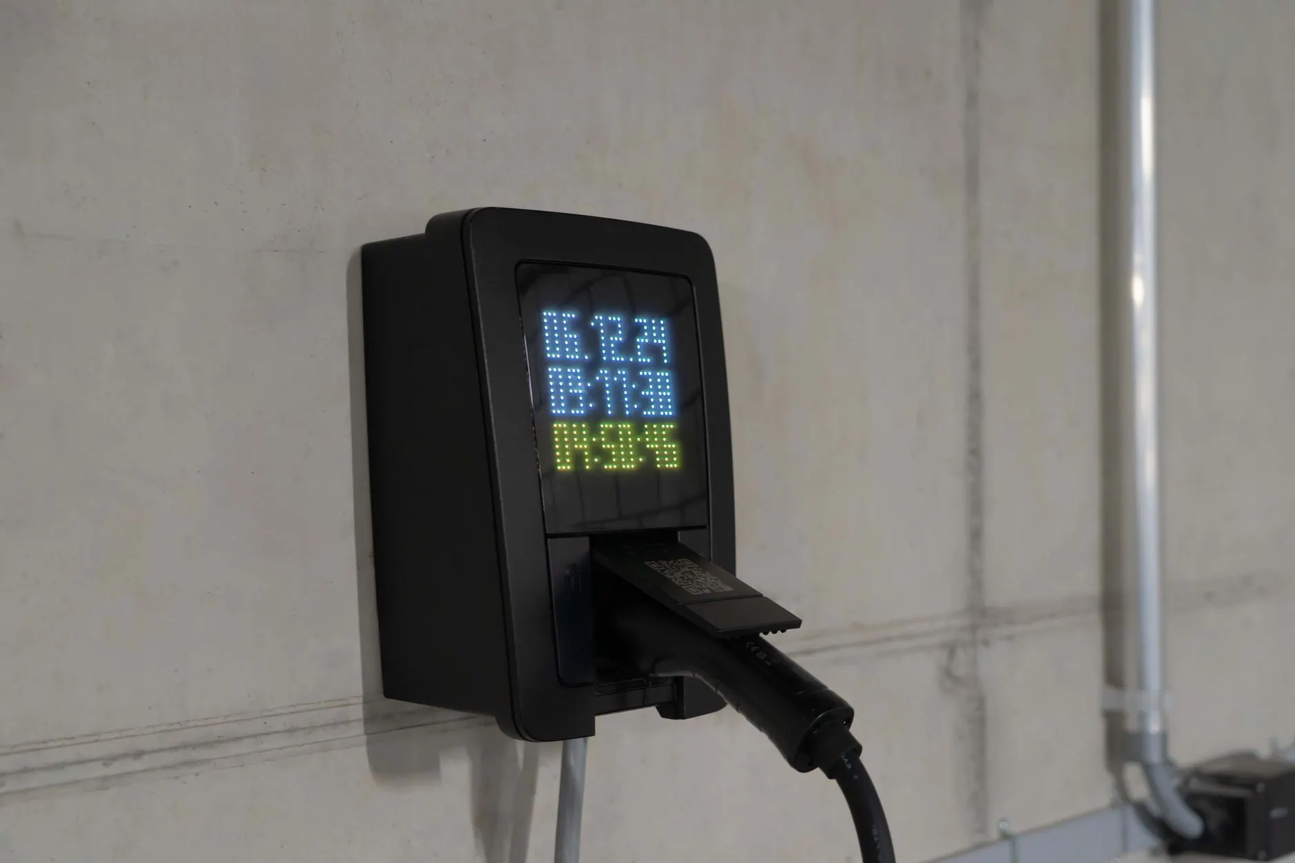 Schwarze Wallbox mit LED-Anzeige an einer Sichtbetonwand, Ladestecker gesteckt