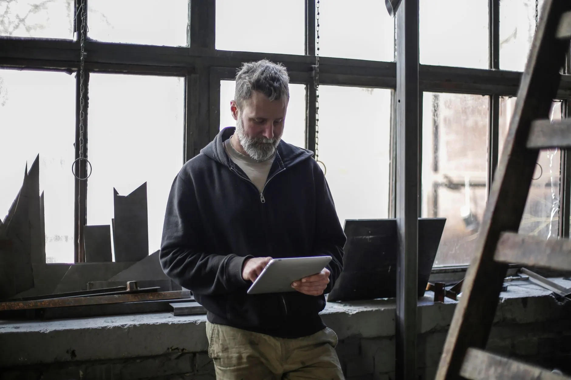 Handwerker mit Tablet vor dem Sprossenfenster einer Werkstatt