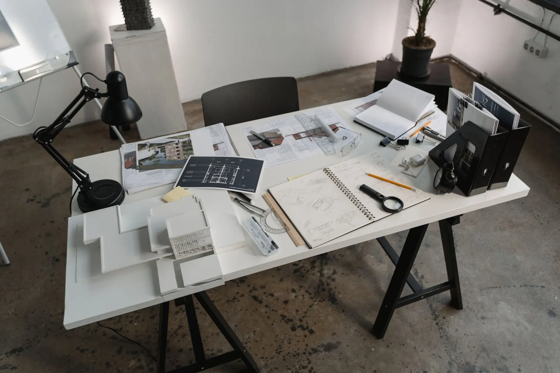 Arbeitstisch mit Plänen, Skizzenblock, Zirkel und Lupe