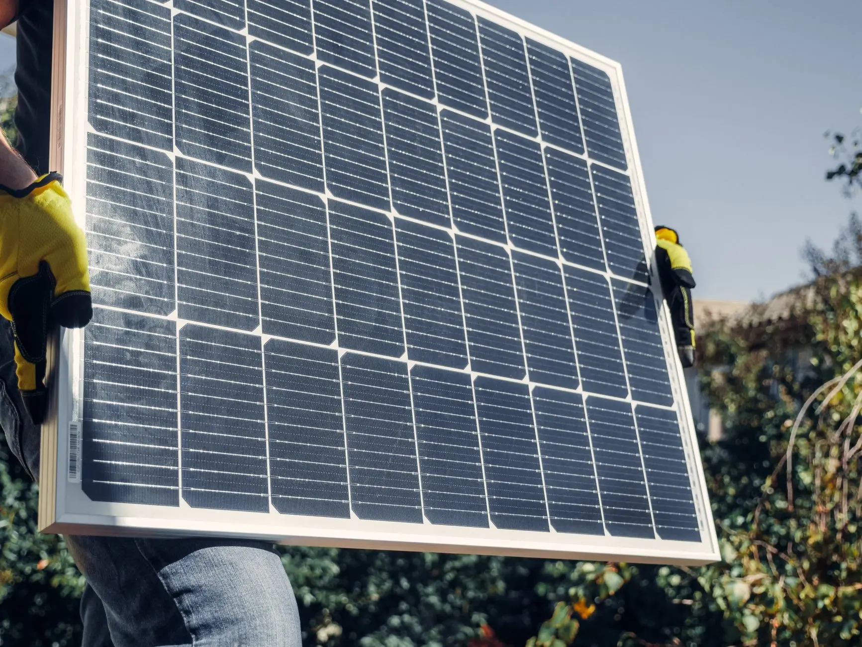 Zwei behandschuhte Hände tragen ein PV-Modul