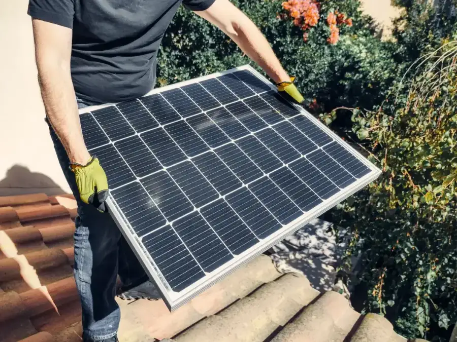 Monteur trägt ein Photovoltaik-Modul auf ein Ziegeldach